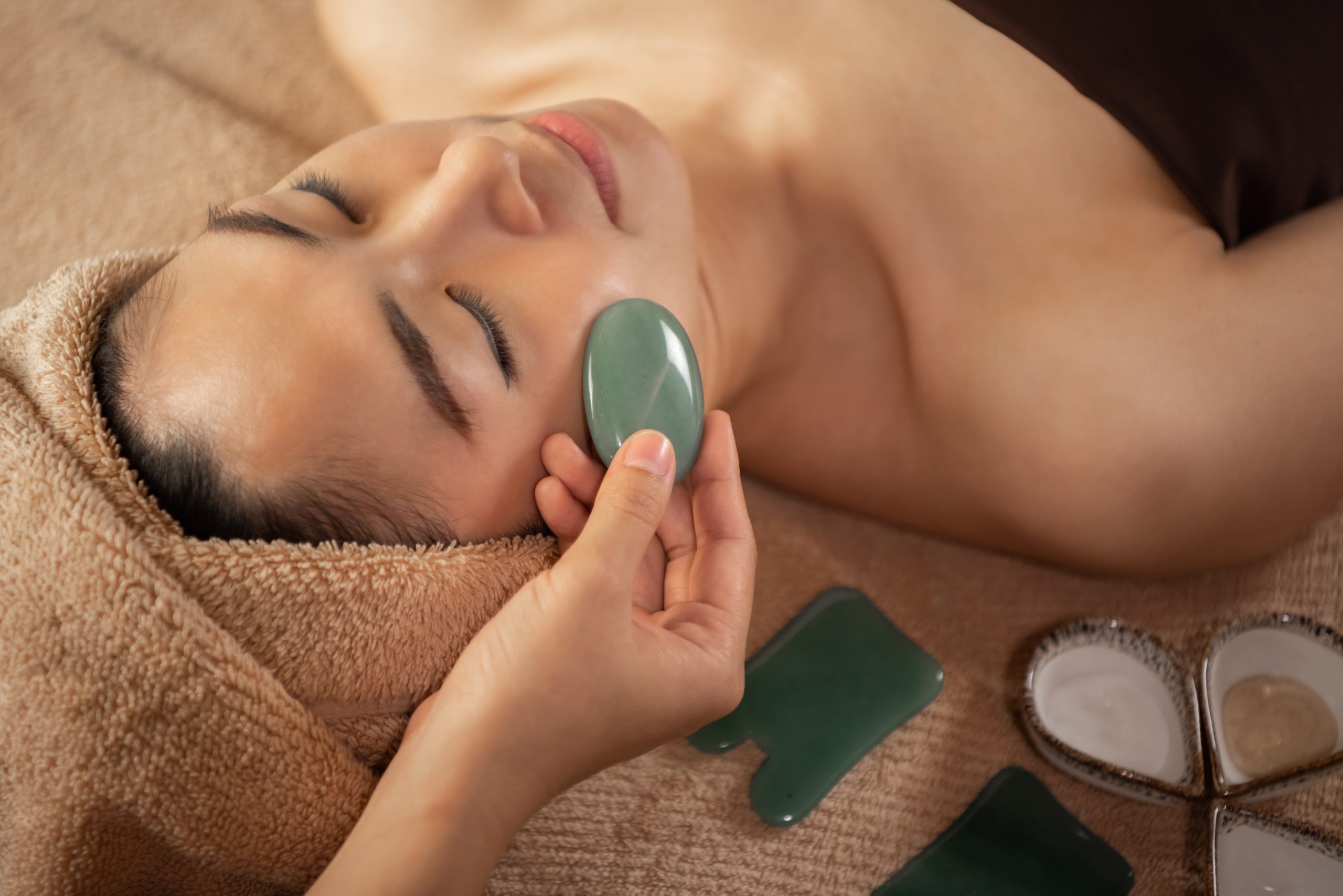 Beautiful Asian female getting Jade Facial Treatment at the Spa Salon. Masseuse hands doing Face Massage.